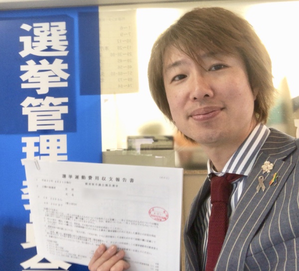 選挙管理委員会の受領印が押された「選挙活動費用収支報告書」を持つフジノ